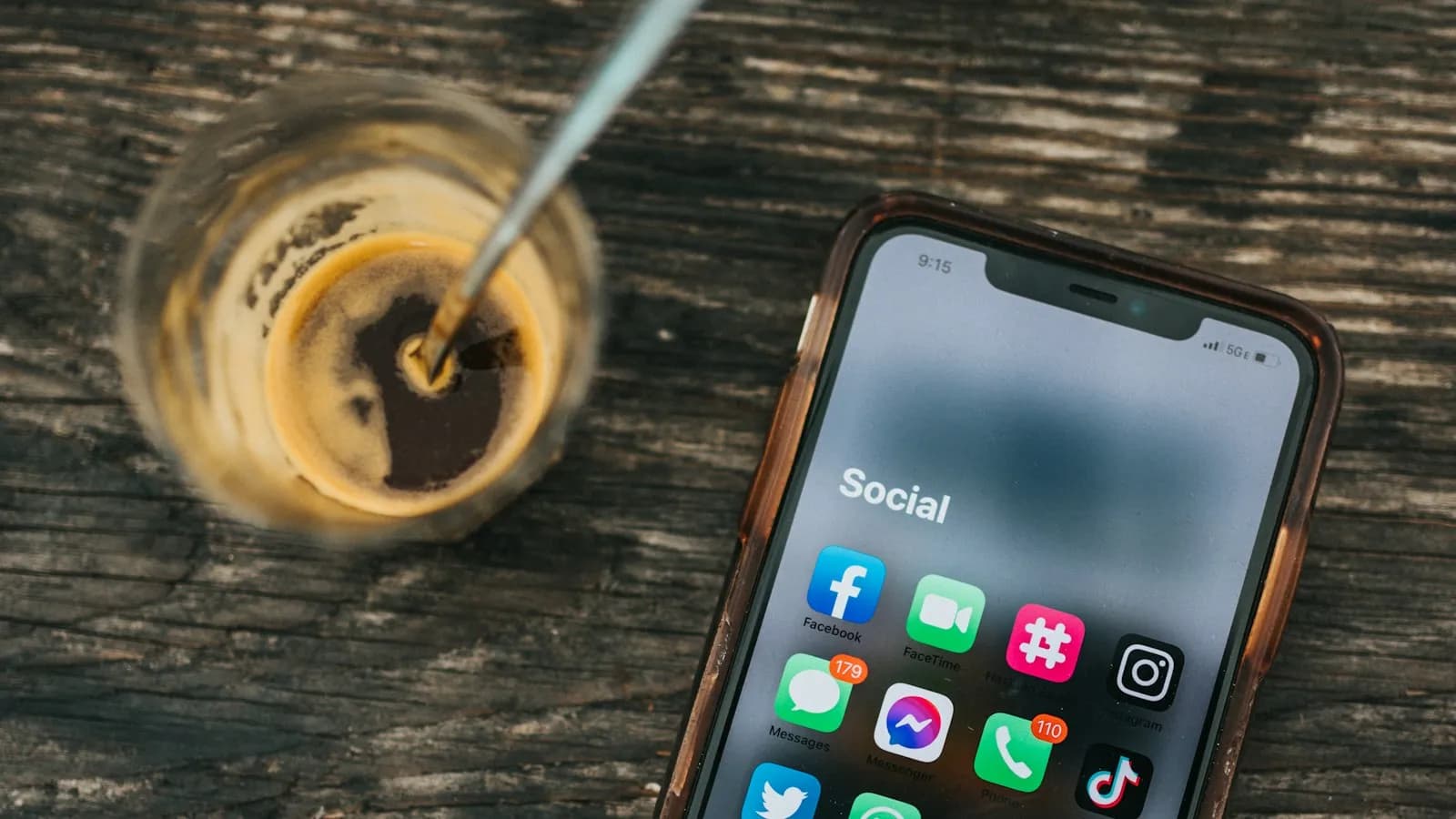 A smartphone showing a folder of social media apps next to a coffee