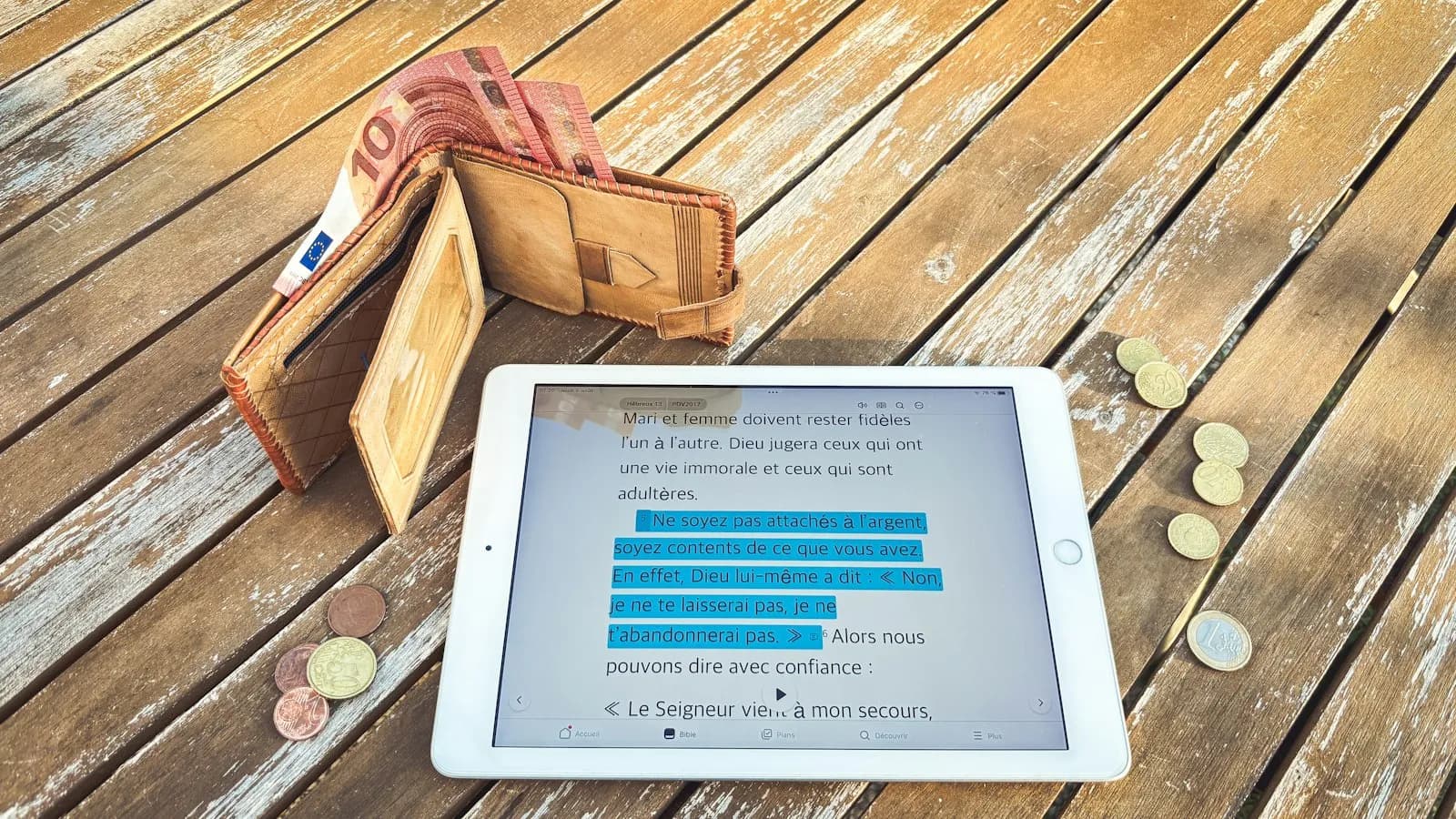 A tablet, a leather wallet with notes and coins on a wooden table