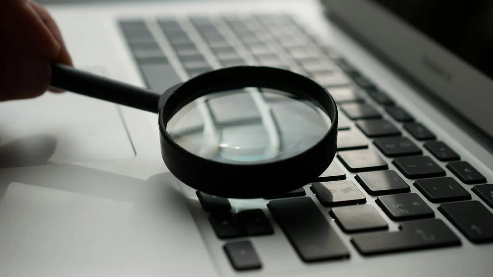 A magnifying glass held over a silver laptop keyboard