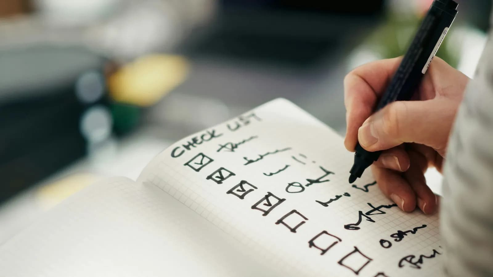 A hand ticking items off a handwritten checklist in a notebook