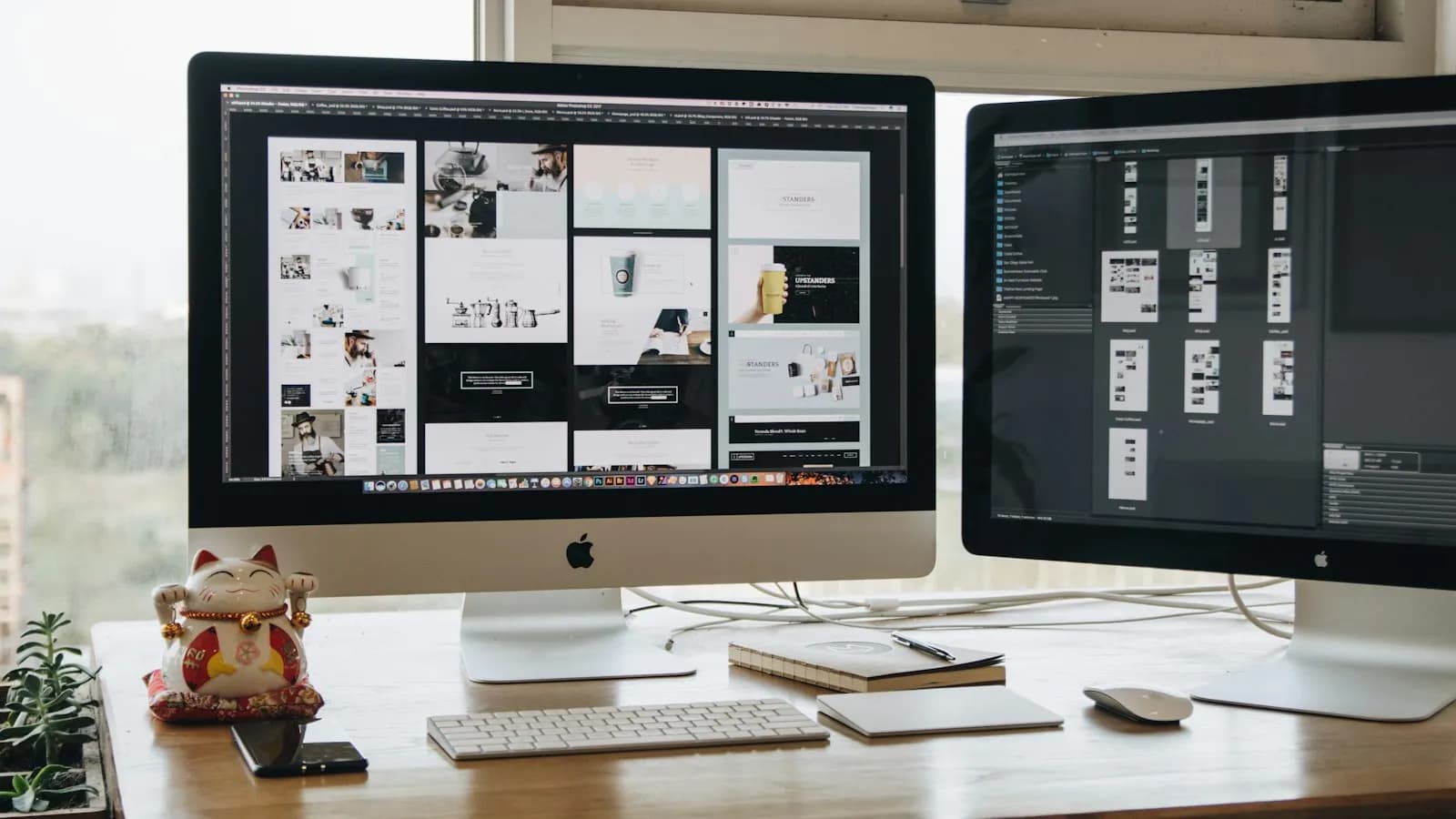 Two large monitors on a wooden desk showing website design layouts